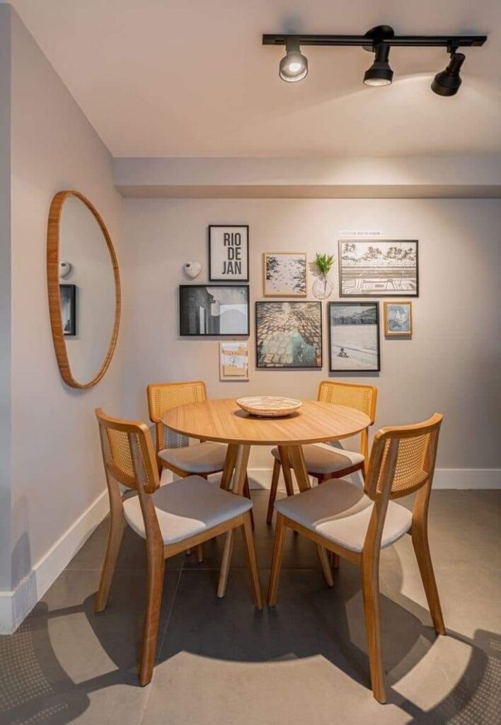 Sala de jantar com mesa redonda de madeira, espelho orgânico e quadros na parede