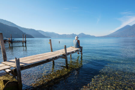 Homem sentado em trapiche de frente para um lago