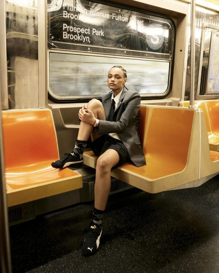 Mulher jovem de pele negra; Ela veste blazer, camisa social, terno, bermuda e tênis Puma Speedcat