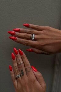 Mãos de pele clara, com anéis em prata e unha amendoada vermelho-tomate