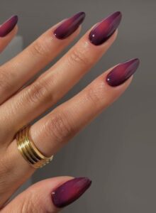 Mão de pele clara, com anel em dourado e unha amendoada com design aura em roxo