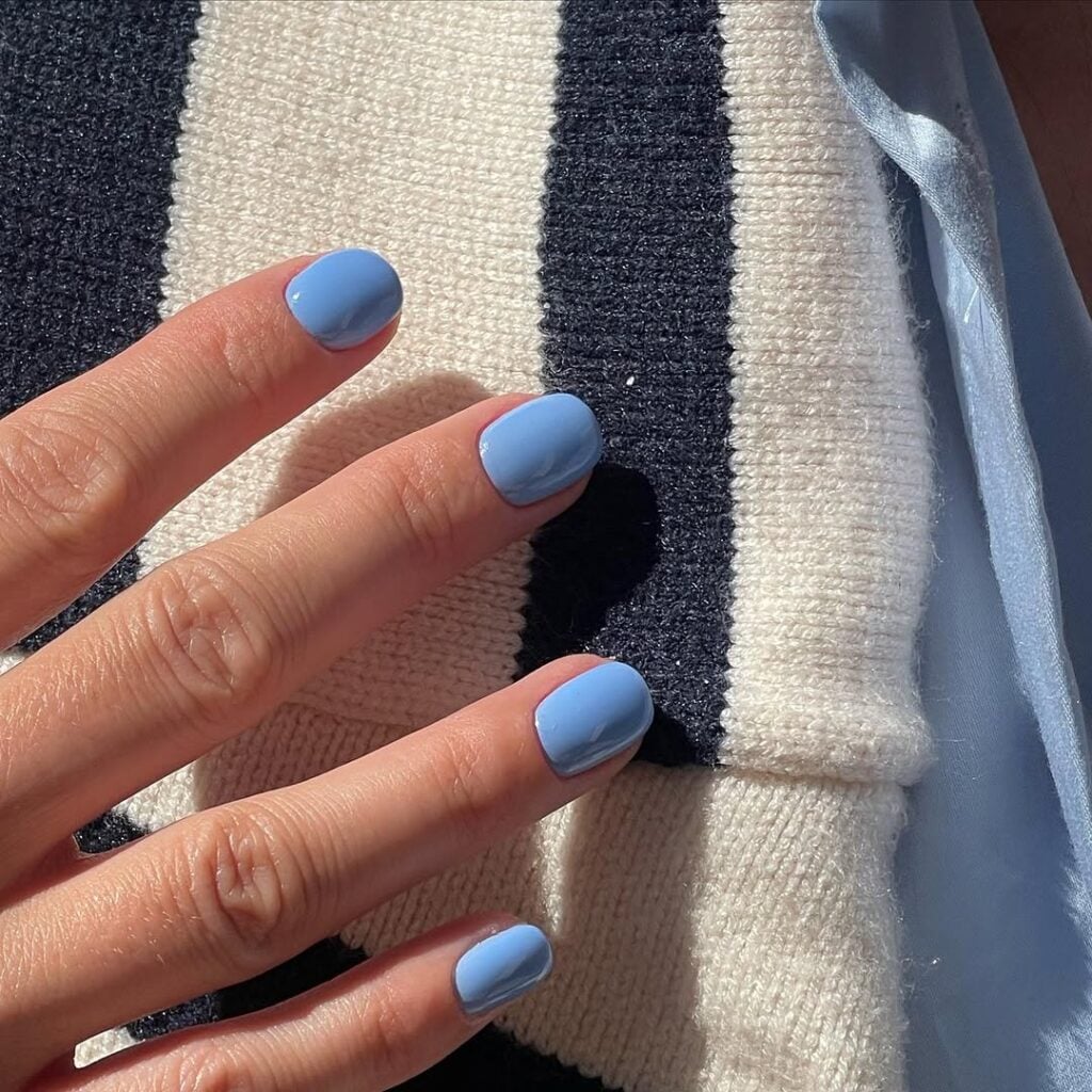 Mão de pele clara, com unha curta squoval azul-bebê
