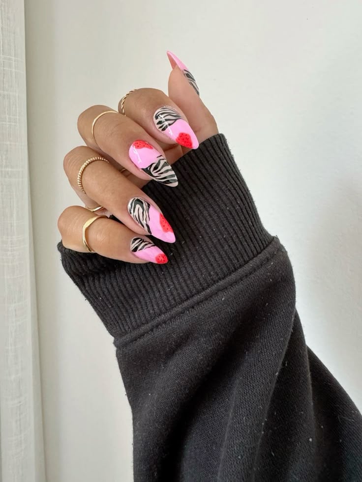 Mão de pele clara, com anéis em dourado e unha amendoada rosa com estampa de zebra 