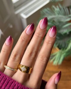 Mão de pele clara, com anéis em dourado e de brilhante e unha amendoada borgonha com francesinha de glitter