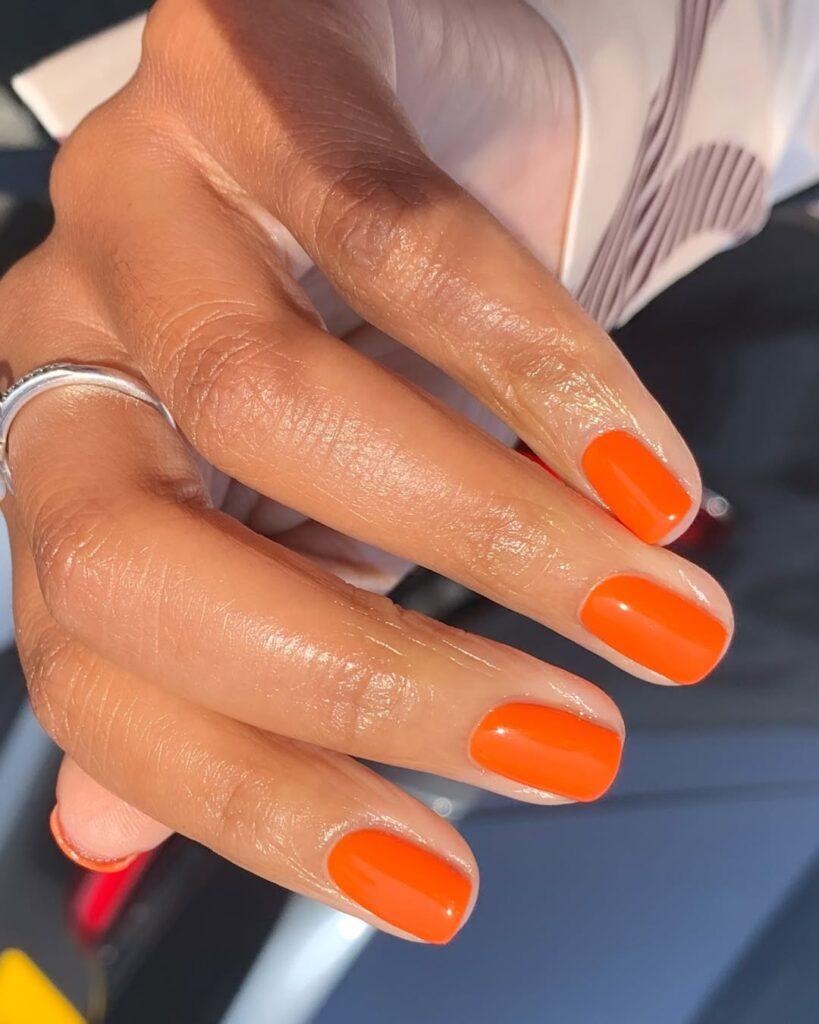 Mão de pele clara, com anel em prata e unha quadrada laranja-tangerina