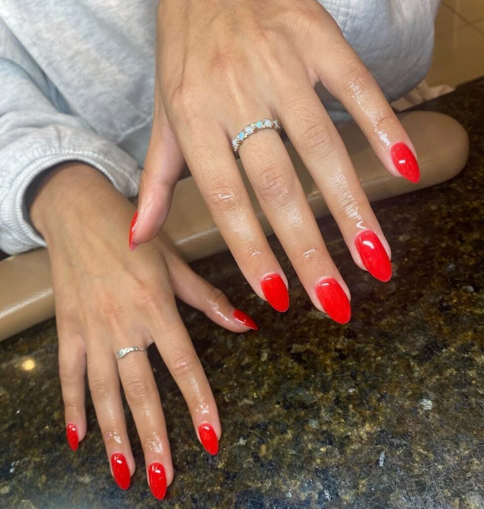 Mãos de pele clara, com anel de brilhante e unha amendoada vermelho-tomate