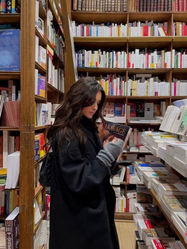 Mulher de pele clara, com cabelo escuro, casaco escuro em uma livraria