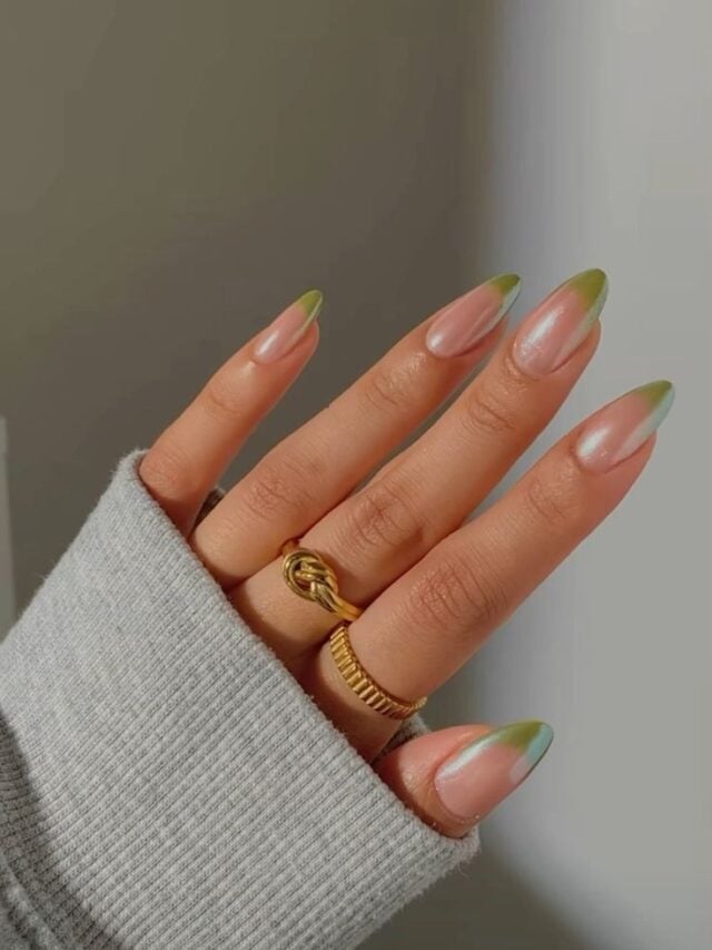 Mão de pele clara, com anéis em dourado e unha amendoada com francesinha verde-claro e acabamento cromado