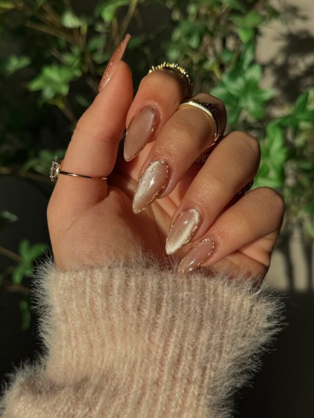 Mão de pele clara, com anéis em dourado e unha amendoada com estilo cat eye e decorações em dourado