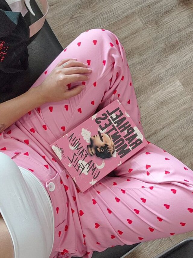 Mulher de pele clara, com blusa branca, calça rosa com corações e o livro Uma família feliz, do Raphael Montes