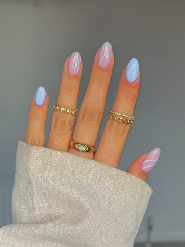 Mão de pele clara, com anéis em dourado e unha amendoada azul-claro com linhas fluidas para decorar