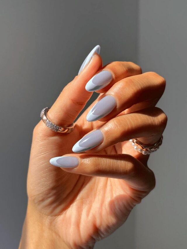 Mão de pele clara, com acessórios em prata e dourado e unha amendoada azul com francesinha monocromática
