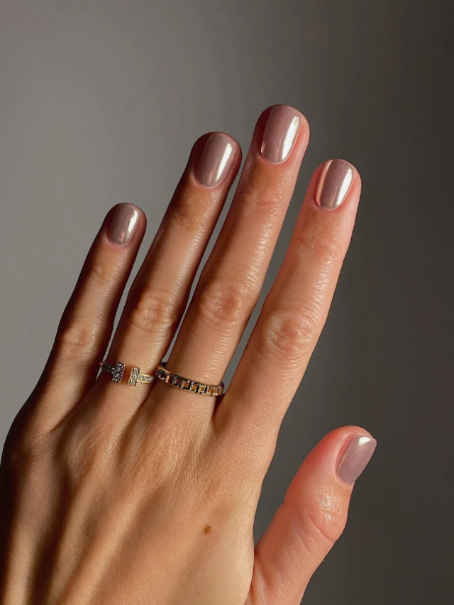 Mão de pele clara, com anéis em dourado e unha curtinha nude metálico