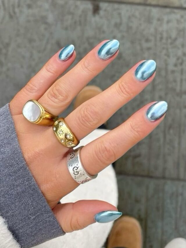 Mão de pele clara, com anéis em dourado e prata e unha redonda azul metalizada