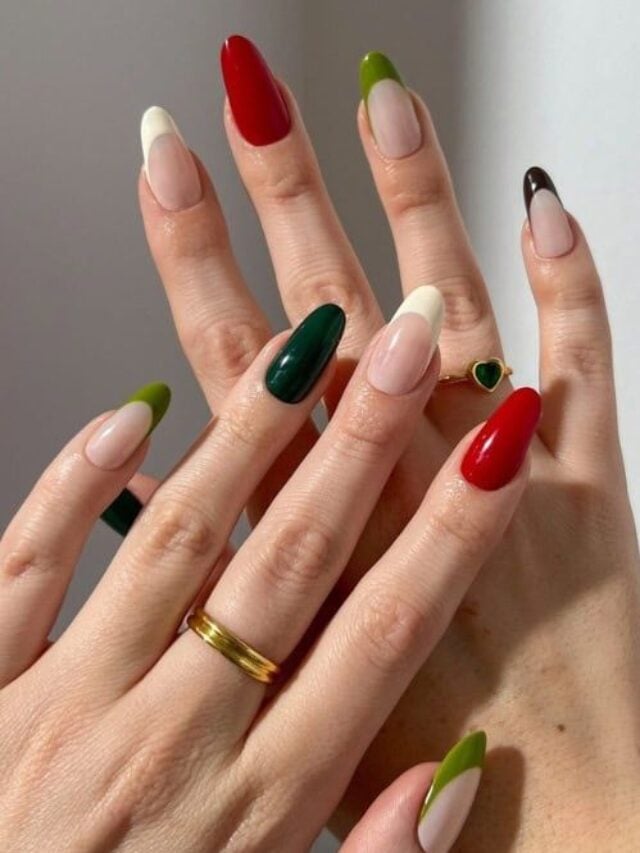 Mãos de pele clara, com anéis em dourado e unhas amendoada em tons de verde, vermelho e branco, com francesinha