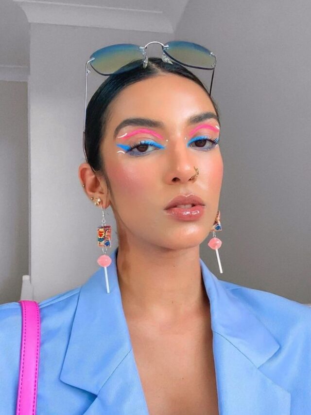 Mulher jovem com pele clara. Ela usa blazer azul e maquiagem colorida para o Carnaval 2025.