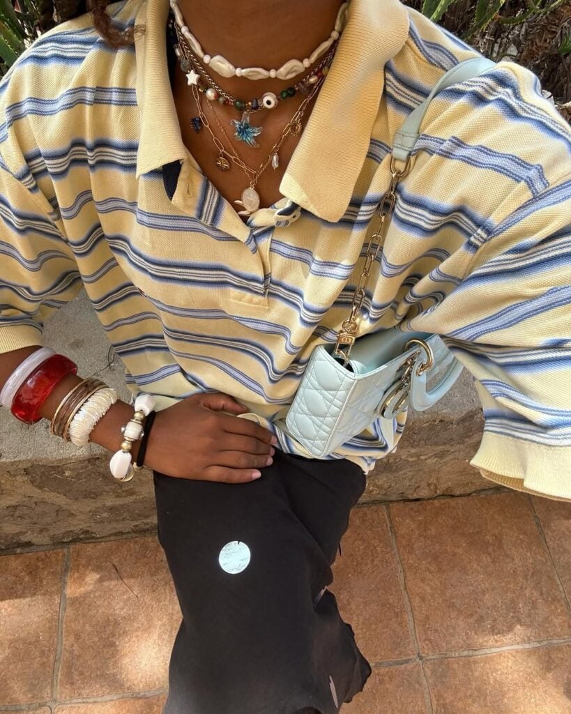 Foto de tronco de mulher de pele escura com camiseta amarela com listras azuis estilo fisherman