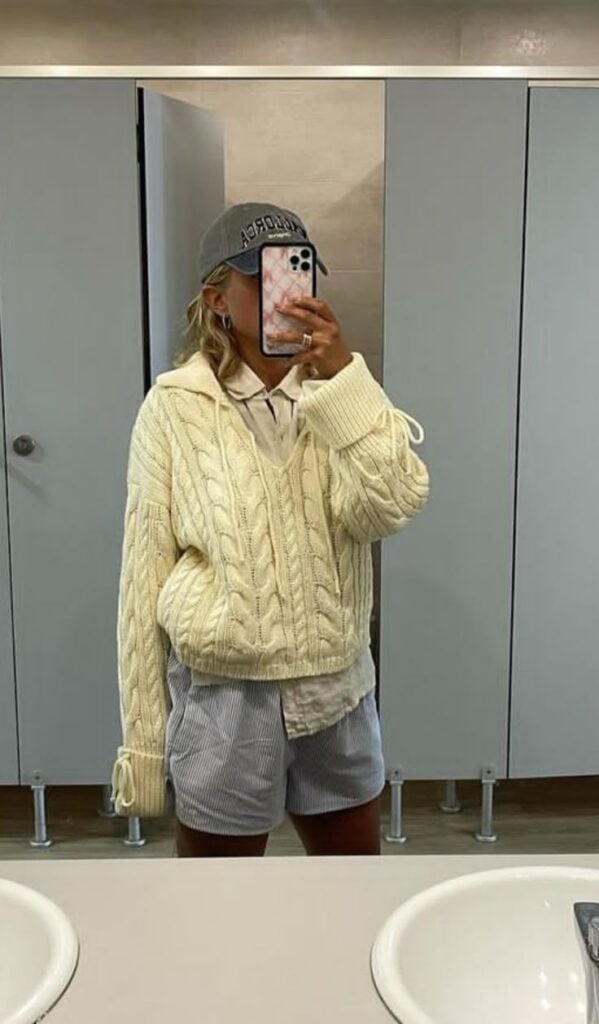 Mulher jovem e magra com suéter amarelo e bermuda azul.