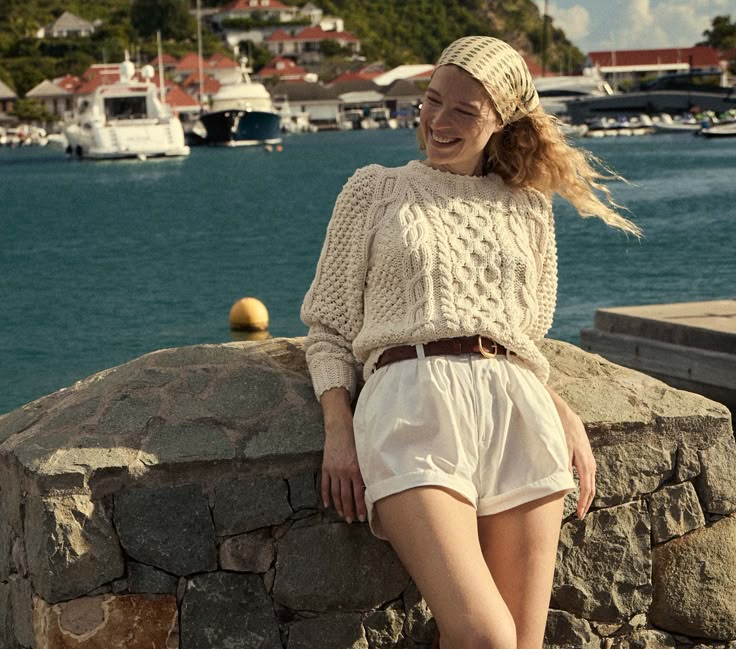 Mulher jovem e magra vestida na estética fisherman core. Ela está com suéter e bermuda.