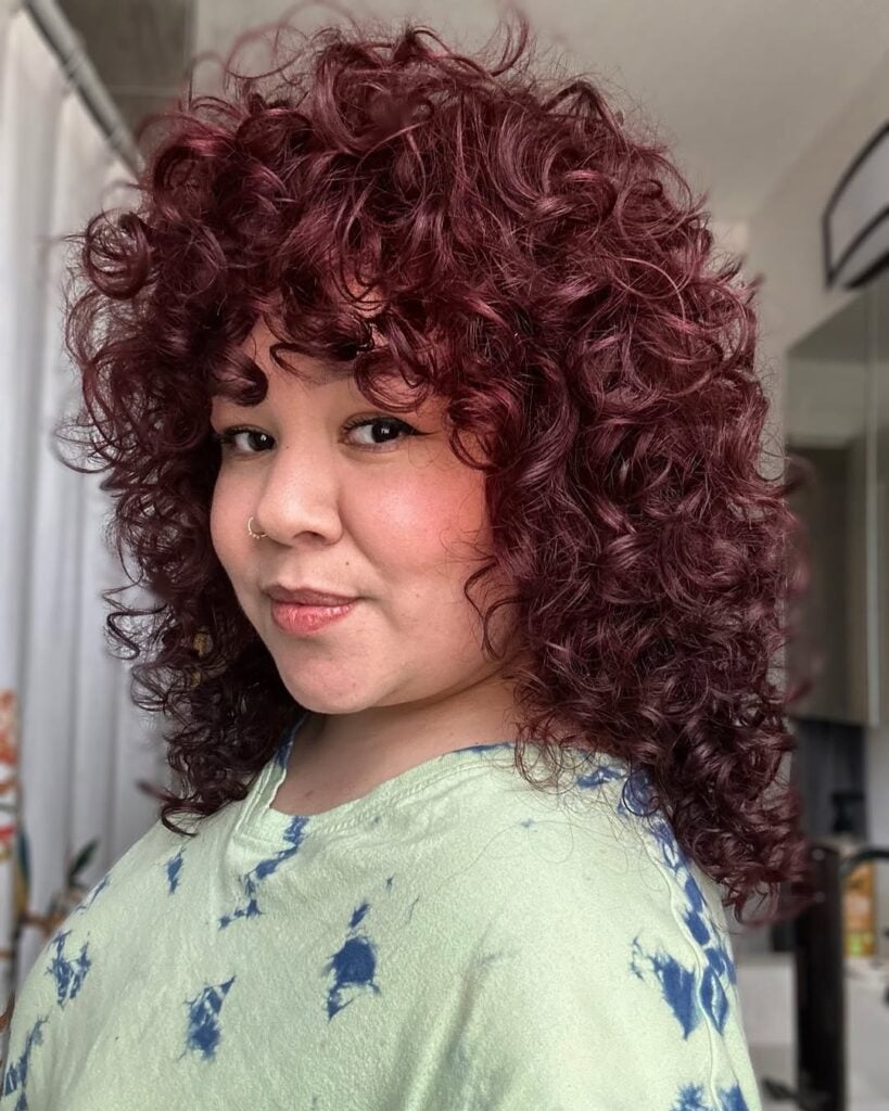 Mulher de pele clara, com blusa verde-claro estampada e cabelo cacheado com a cor cherry cola