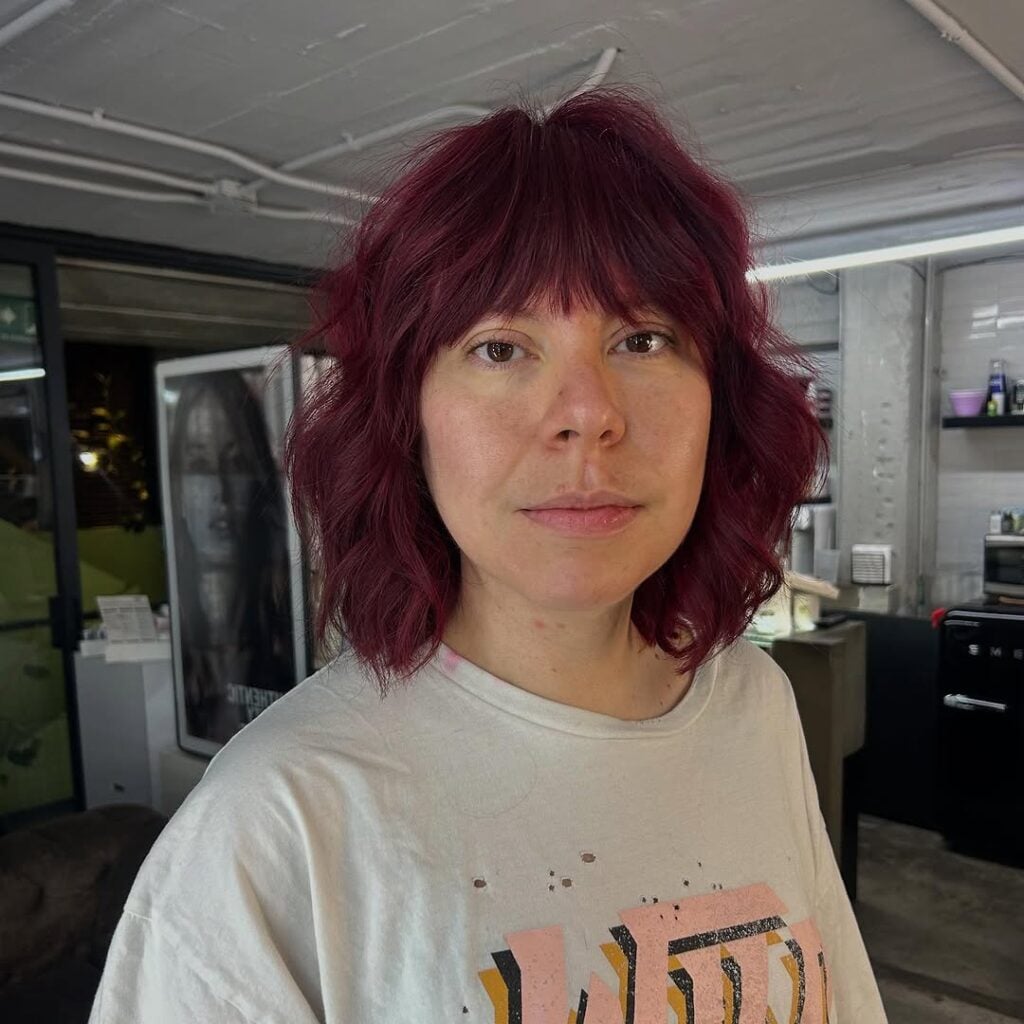 Mulher de pele clara, com blusa branca estampada e cabelo curto com franja cherry cola 