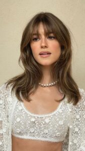 Daisy Edgar-Jones, com conjunto branco com renda, colar de pérola e cabelo castanho médio com franja