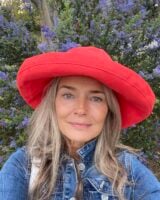 Mulher de pele branca e madura, com cabelo natural, jaqueta jeans e chapéu vermelho