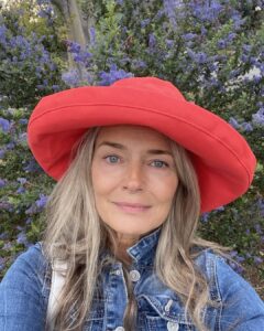 Mulher de pele branca e madura, com cabelo natural, jaqueta jeans e chapéu vermelho