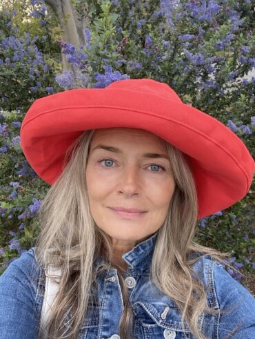 Mulher de pele branca e madura, com cabelo natural, jaqueta jeans e chapéu vermelho