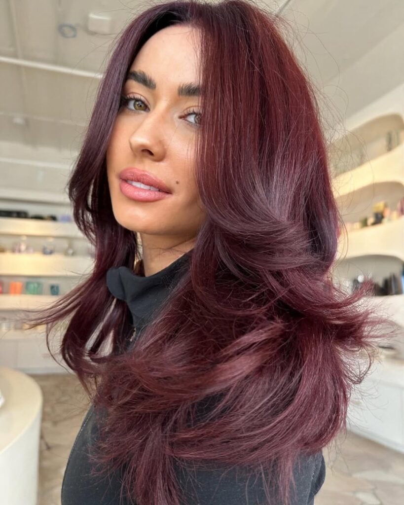 Mulher de pele clara, com blusa preta e cabelo em camadas cherry cola 