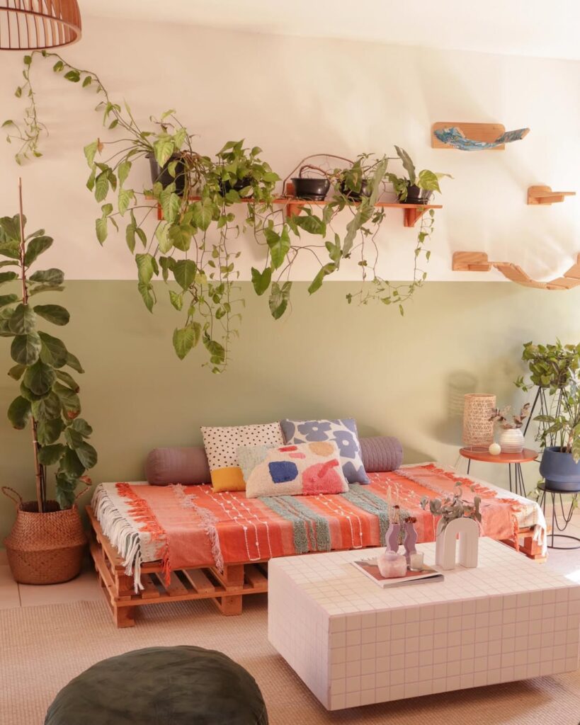 Sala de estar com sofá feito de pallet, meia parede em verde e prateleira com plantas