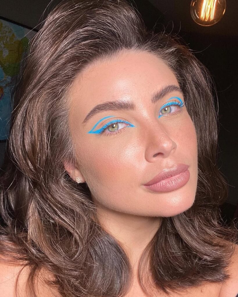 Mulher de pele clara, com cabelo castanho e maquiagem com delineado gráfico azul 