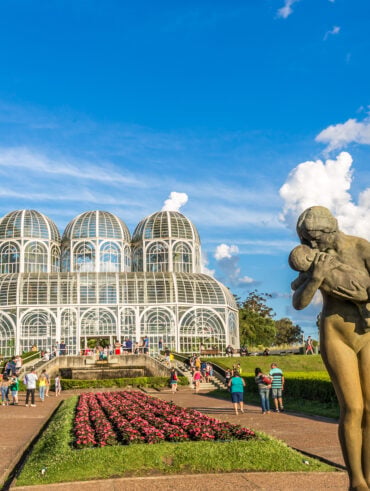 Paisagem com céu azul e em primeiro plano uma escultura de uma mulher segurando um bebê