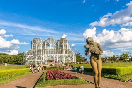 Paisagem com céu azul e em primeiro plano uma escultura de uma mulher segurando um bebê