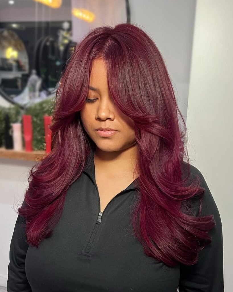 Mulher de pele 'média', blusa preta e cabelo em camadas cherry cola 