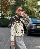 Mulher de pele clara, com calça jeans, cabelo loiro preso e jaqueta com estampa de vaca