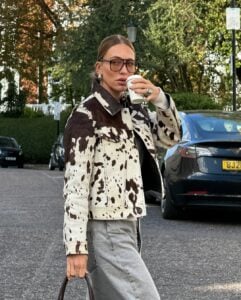 Mulher de pele clara, com calça jeans, cabelo loiro preso e jaqueta com estampa de vaca