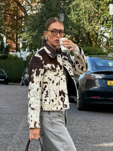 Mulher de pele clara, com calça jeans, cabelo loiro preso e jaqueta com estampa de vaca