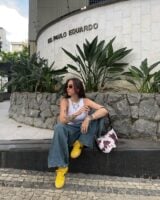 Mulher de pele clara, com jeans e blusa branca, tênis amarelo e bolsa com estampa de vaca