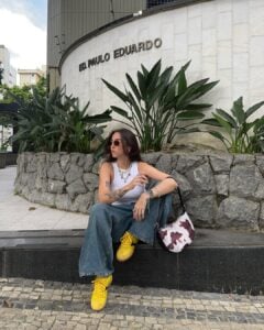 Mulher de pele clara, com jeans e blusa branca, tênis amarelo e bolsa com estampa de vaca