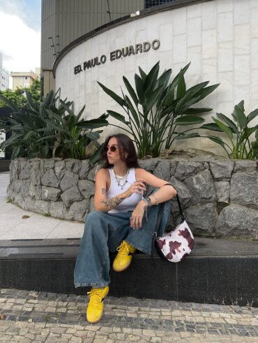Mulher de pele clara, com jeans e blusa branca, tênis amarelo e bolsa com estampa de vaca
