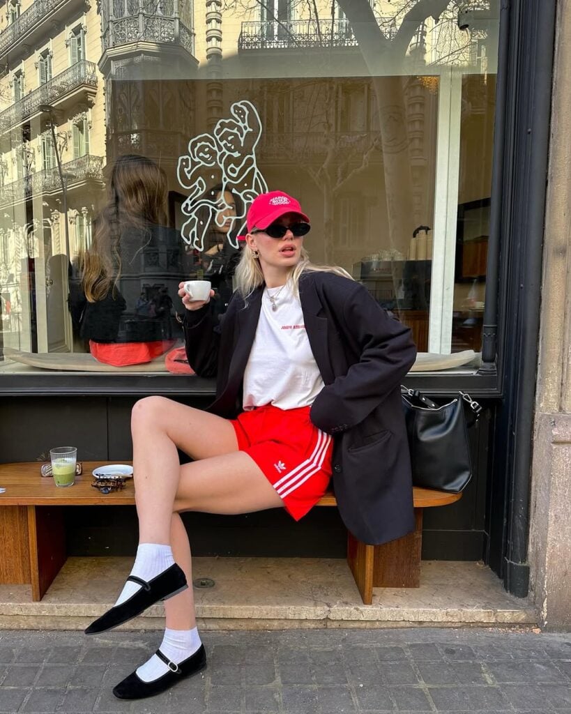 Mulher jovem e magra com camiseta, bermuda, blazer e sapatilha com meia.