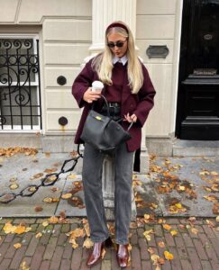 Mulher de pele clara, com calça jeans cinza, blazer e pulover ameixa.