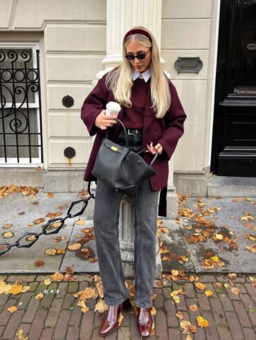 Mulher de pele clara, com calça jeans cinza, blazer e pulover ameixa.