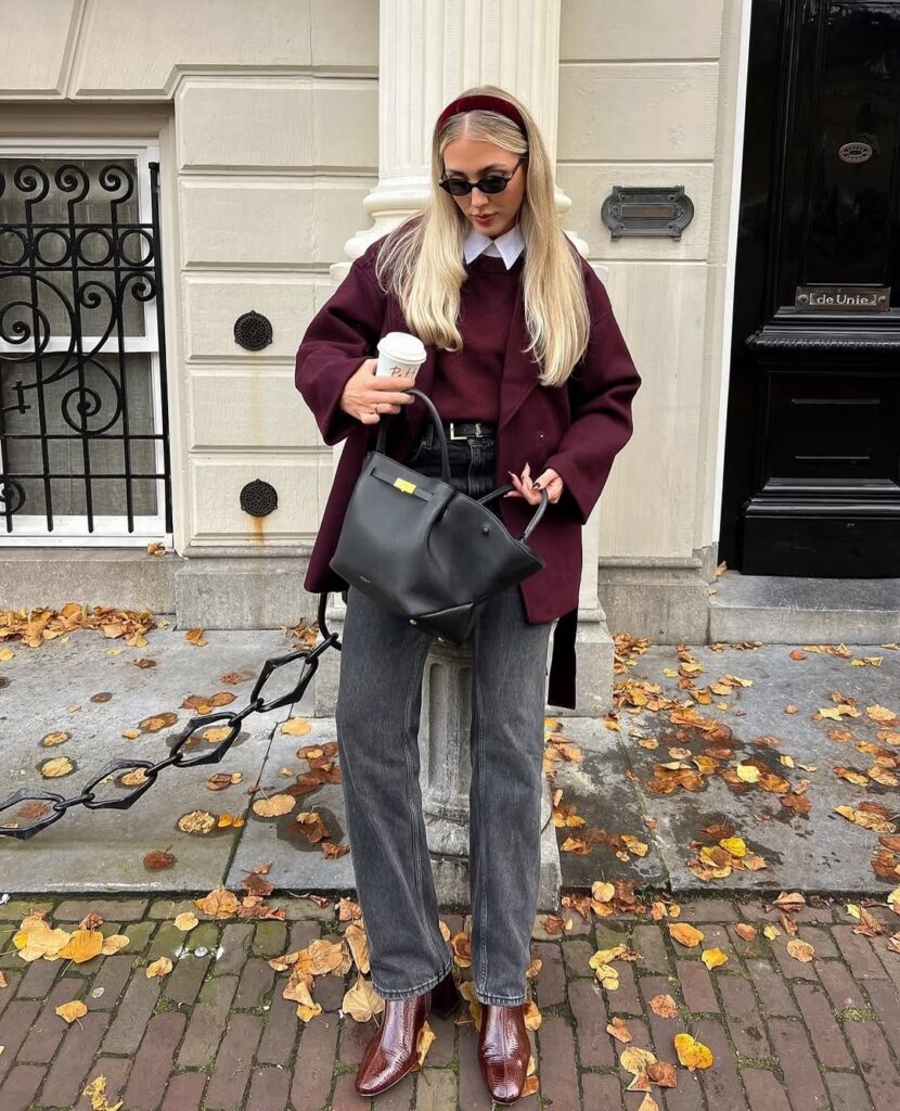 Mulher de pele clara, com calça jeans cinza, blazer e pulover ameixa. 