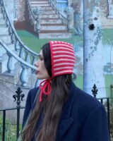 Mulher de pele clara, com casaco azul-marinho, bolsa verde-escuro, cabelo longo e castanho e bonnet listrado