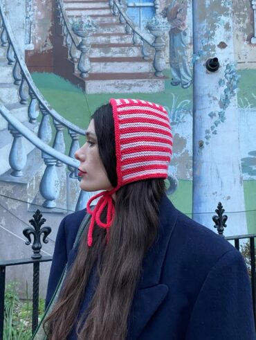 Mulher de pele clara, com casaco azul-marinho, bolsa verde-escuro, cabelo longo e castanho e bonnet listrado