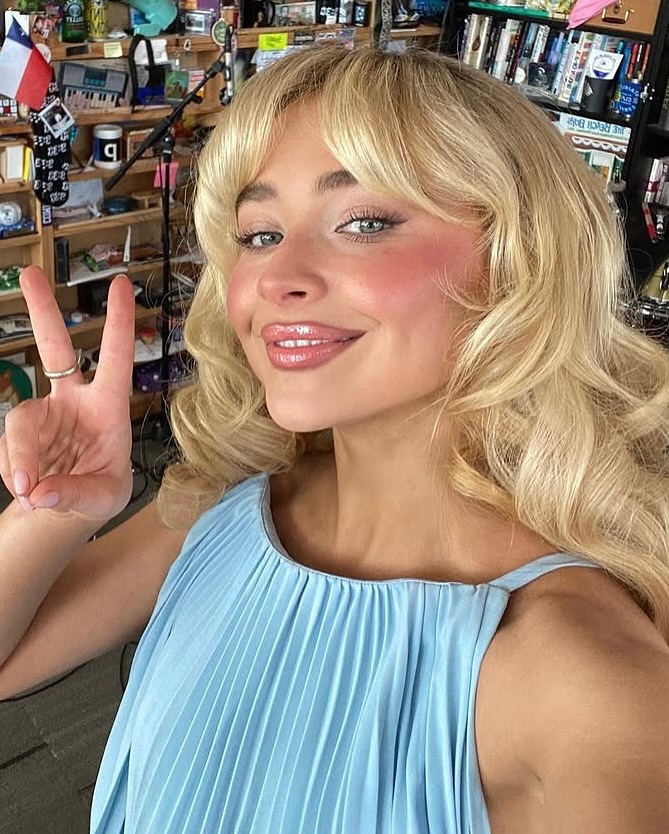 Sabrina Carpenter com vestido azul-claro, cabelo loiro com franja e maquiagem aquarela