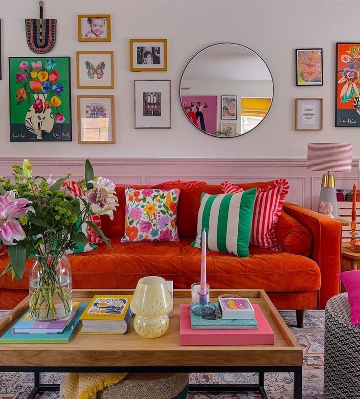 Sala com sofá laranja, quadros e espelho redondo