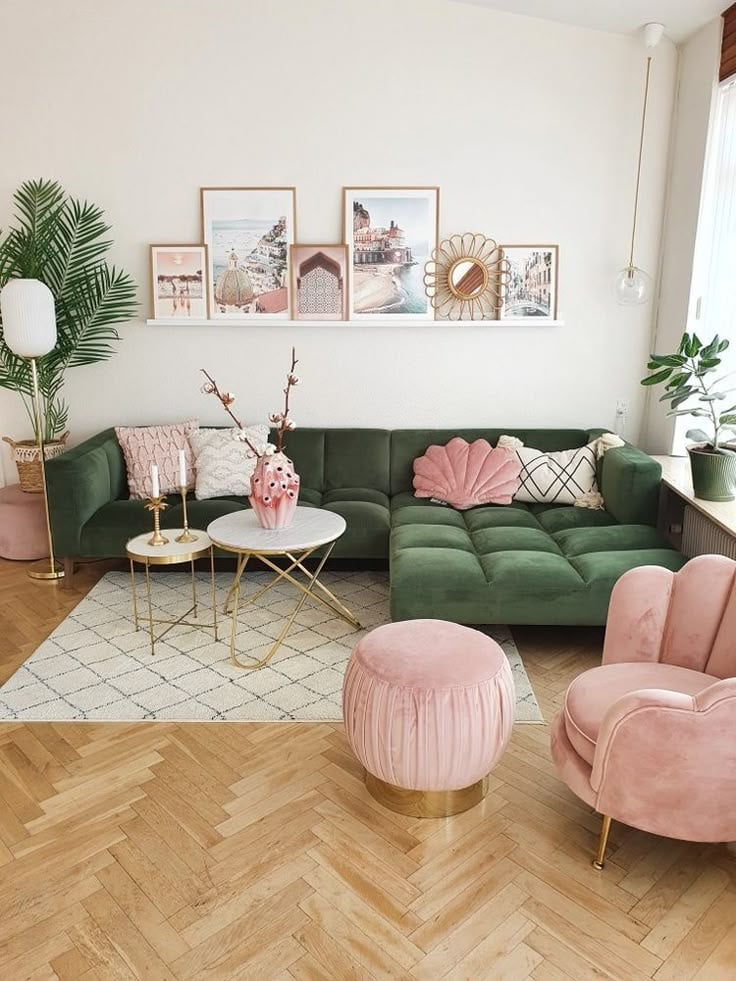 Sala de estar com sofá em veludo verde, poltrona e puff rosa e prateleira com quadros
